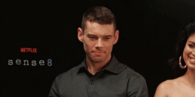 A Man And Woman Are Standing In Front Of A Sign That Says Sense 8 GIF