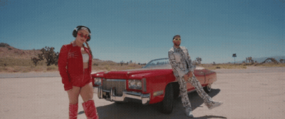 A Man And Woman Are Standing Next To A Red Car GIF