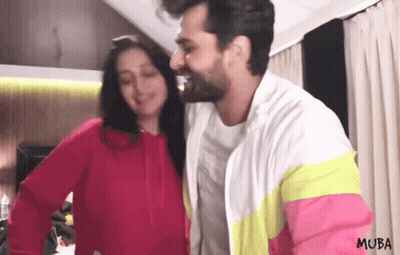 A Man And Woman Are Standing Next To Each Other And The Man Is Wearing A Jacket That Says Muba On It GIF