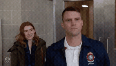 A Man And Woman Are Standing Next To Each Other In A Hallway . GIF