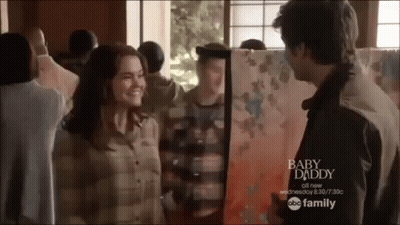 A Man And Woman Are Standing Next To Each Other In Front Of A Painting Titled Baby Daddy GIF