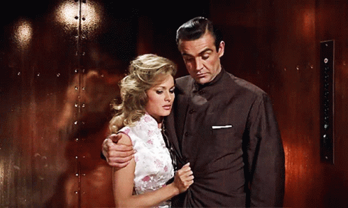 A Man And Woman Are Standing Next To Each Other In Front Of A Red Wall GIF
