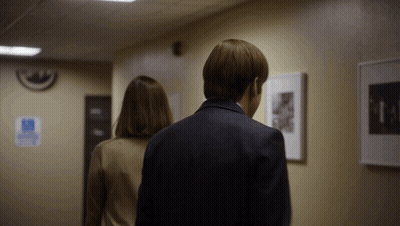 A Man And Woman Are Walking Down A Hallway With A Handicap Sign On The Wall Behind Them GIF
