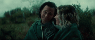 A Man And Woman Are Wrapped In A Green Blanket And Looking At Each Other GIF