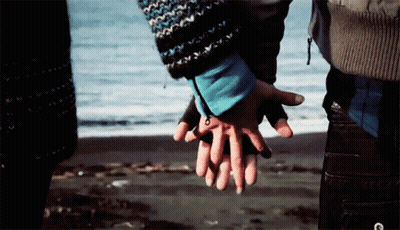 A Man And Woman Holding Hands On The Beach GIF