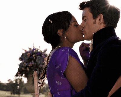 A Man And Woman Kissing In Front Of Flowers GIF