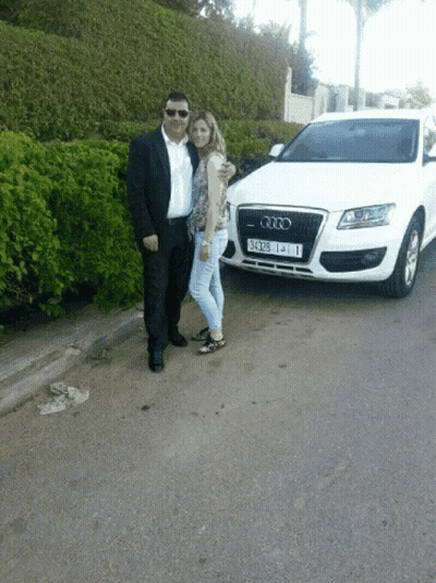 A Man And Woman Posing In Front Of An Audi GIF