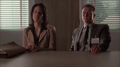 A Man And Woman Sit At A Table With A Visitor Tag GIF