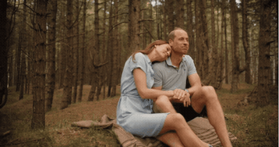 A Man And Woman Sit On A Blanket In The Woods Holding Hands GIF