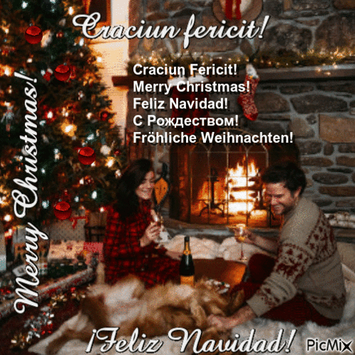 A Man And Woman Sitting In Front Of A Fireplace With A Christmas Tree In The Background GIF