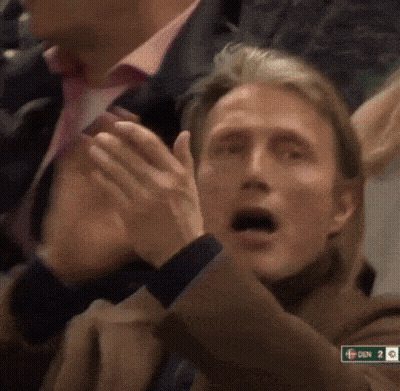 A Man Applauds While Sitting In A Crowd With A Sign That Says Den On It GIF
