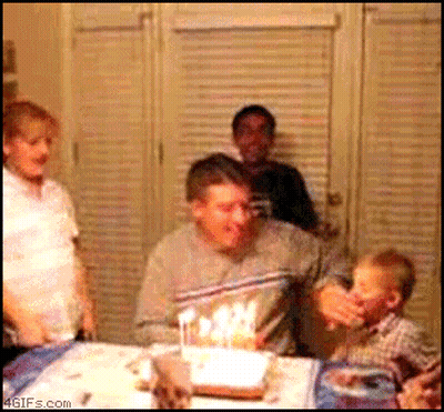 A Man Blows Out Candles On A Birthday Cake While A Child Watches GIF