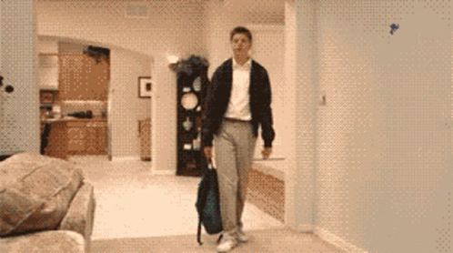 A Man Carrying A Backpack Walks In A Living Room GIF