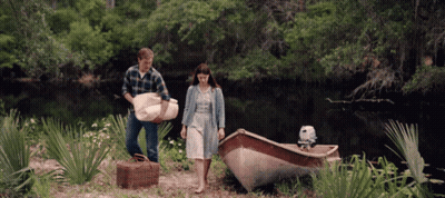 a man carrying a blanket and a woman carrying a picnic basket next to a small boat
