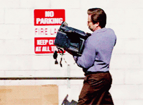 A Man Carrying A Box In Front Of A Sign That Says No Parking Fire Lane GIF