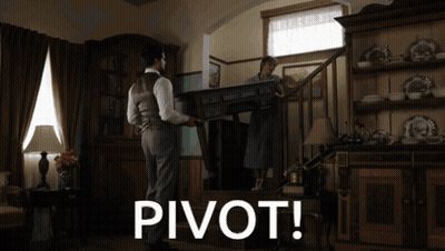 A Man Carrying A Table In A Living Room With The Word Pivot Below Him GIF