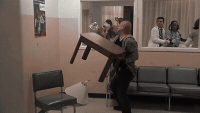 A Man Carrying A Table In A Waiting Room With A Red Cross Sign On The Wall GIF