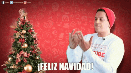 A Man Clapping In Front Of A Christmas Tree With The Words Feliz Navidad Written Below Him GIF