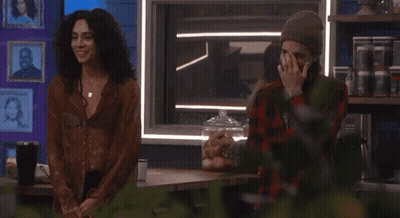 A Man Covering His Face While Standing Next To A Woman In A Plaid Shirt GIF