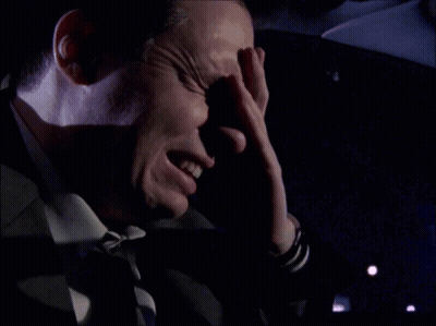A Man Covering His Face With His Hand In A Dark Room GIF