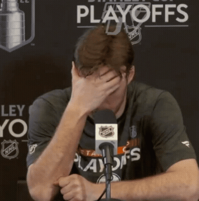 A Man Covering His Face With His Hand In Front Of A Playoffs Banner GIF