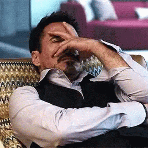 A Man Covering His Face With His Hand While Laying On A Couch GIF