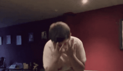 A Man Covering His Face With His Hands In A Room With Red Walls GIF
