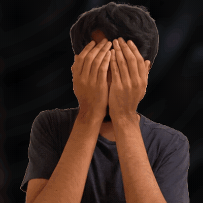 A Man Covering His Face With His Hands In Front Of A Black Background GIF