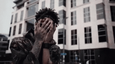 A Man Covering His Face With His Hands In Front Of A Building . GIF
