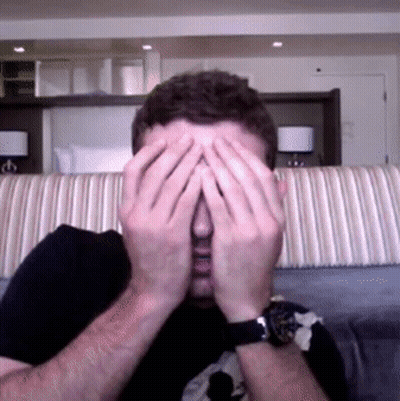 A Man Covering His Face With His Hands In Front Of A Couch GIF