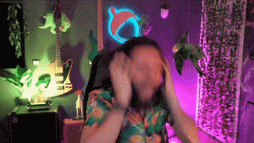 A Man Covering His Face With His Hands In Front Of A Guitar And A Neon Sign GIF
