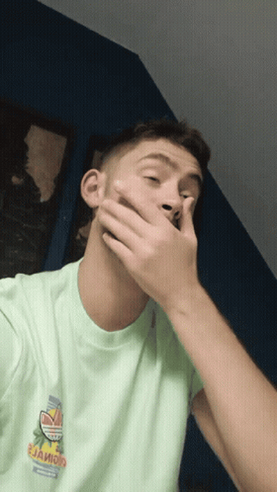A Man Covering His Mouth With His Hand And Wearing A Green Shirt That Says " Jaioio " GIF
