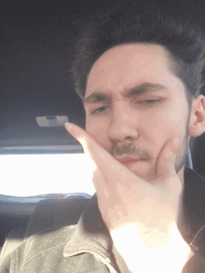 A Man Covering His Mouth With His Hand While Wearing A Black Jacket GIF