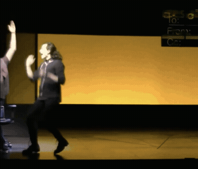 A Man Dancing On A Stage In Front Of A Screen That Says " To : From " GIF