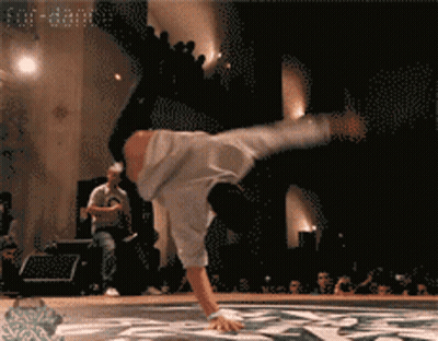 A Man Doing A Handstand On A Stage With A Crowd Watching GIF