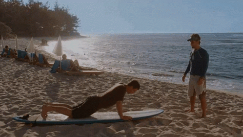 A Man Doing Push Ups On A Surfboard While Another Man Watches GIF