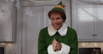 A Man Dressed As A Christmas Elf Is Smiling In A Kitchen GIF