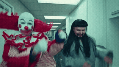 A Man Dressed As A Clown And Another Man Dressed As A Prisoner Are Dancing In A Hallway GIF