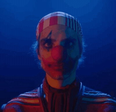 A Man Dressed As A Clown With A Red Nose And A Striped Headband On His Head . GIF