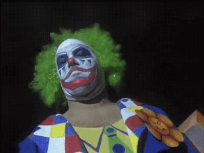 A Man Dressed As A Clown With A Teddy Bear Pinned To His Chest GIF