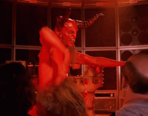 A Man Dressed As A Devil With Horns Is Standing In A Room . GIF