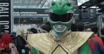 A Man Dressed As A Green Power Ranger Stands In A Crowd Of People GIF