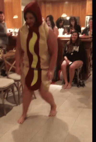 A Man Dressed As A Hot Dog Is Dancing In Front Of A Crowd GIF