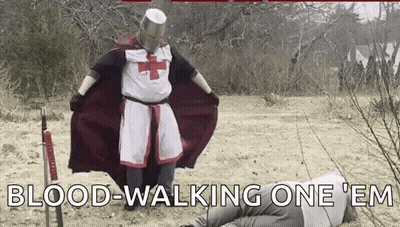 A Man Dressed As A Knights Templar Is Standing Next To A Man Laying On The Ground With A Sword . GIF