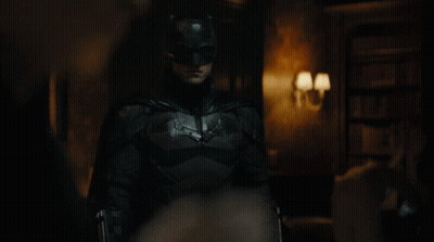 A Man Dressed As Batman Stands In A Dark Room GIF