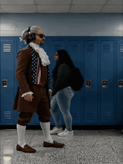 A Man Dressed As Benjamin Franklin Is Walking In A Hallway With Blue Lockers GIF