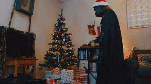 A Man Dressed As Darth Vader Standing In Front Of A Christmas Tree GIF