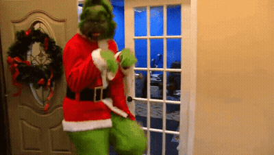 A Man Dressed As Grinch Is Standing In A Doorway . GIF