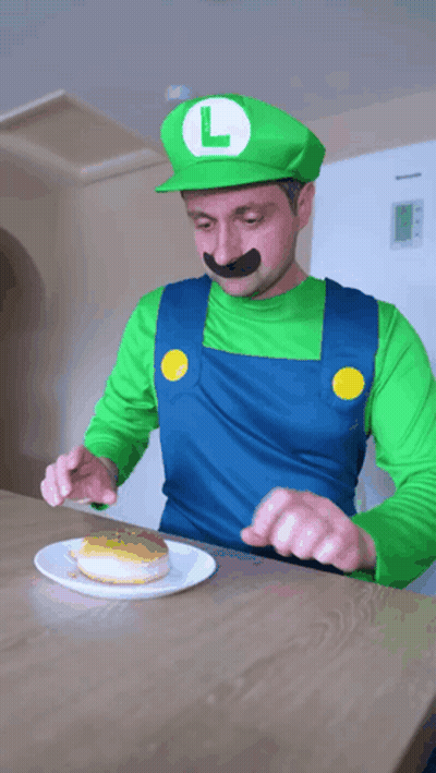 A Man Dressed As Luigi From Super Mario Is Eating A Donut GIF