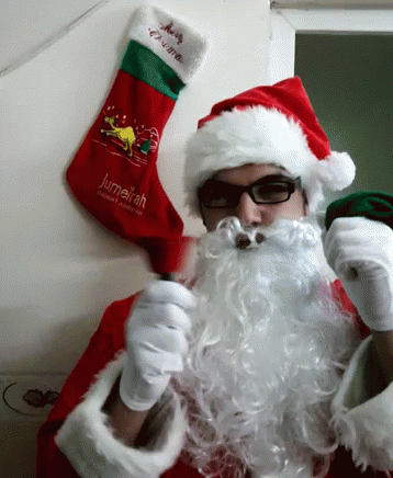A Man Dressed As Santa Claus Holds A Christmas Stocking That Says Jumelah GIF